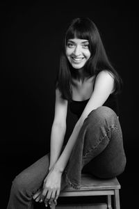 Portrait of smiling woman sitting against black background