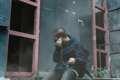 Young man wearing mask listening music while sitting outdoors