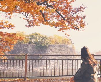 Rear view of woman standing by railing during autumn