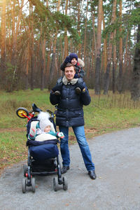 Full length portrait of happy siblings on bicycle against trees