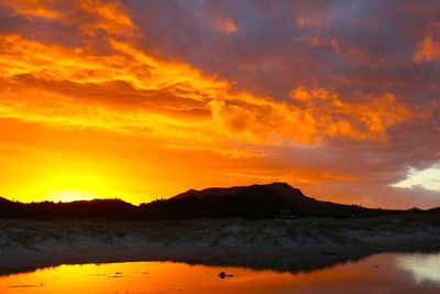 Silhouette mountain by lake against cloudy sky during sunset