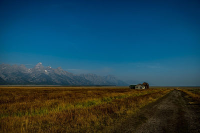 Road amidst field against blue sky