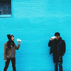 Man and woman using cups and string to communicate against blue wall