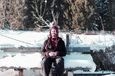 Full length portrait of woman sitting in park during winter
