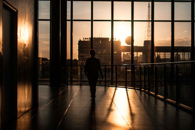 Silhouette woman walking in corridor of modern building against sunset