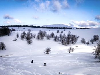 Scenic view of snowcapped mountain against sky and snowboarders on the slope