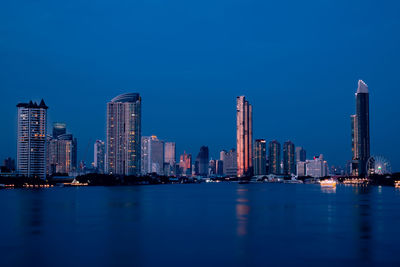 Illuminated buildings in city against blue sky