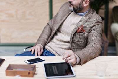 Midsection of businessman with digital tablet and smart phone sitting at table in creative office