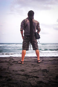 Rear view of man standing at beach against sky