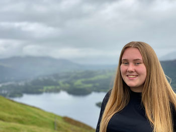 Portrait of smiling young woman standing on a mountain against sky