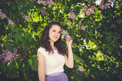 Happy curly hair young woman in a white t-shirt under the blooming lilac trees. smiling
