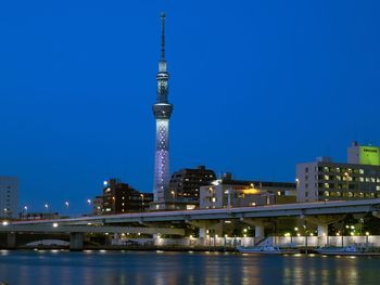 Illuminated bridge over river by buildings against sky at night