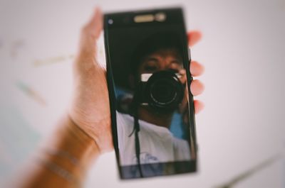 Reflection of man holding camera on mobile screen