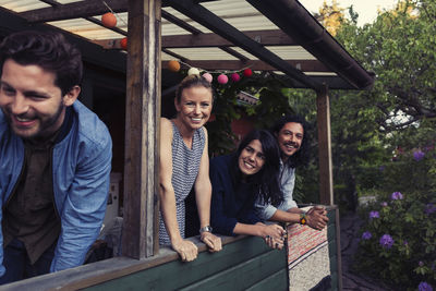 Portrait of happy young woman standing with friends on porch at log cabin