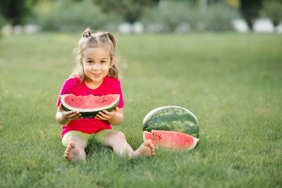 Funny cute child girl 3-4 year old eating ripe watermelon on green grass outdoor. 