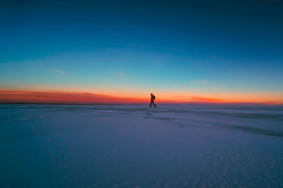 Man walking on snowy landscape against sky during sunset
