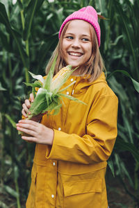 Stylish teenage girl in yellow raincoat and hot pink hat laughing on corn field