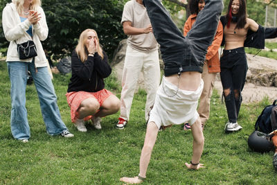 Male teenager doing handstand by friends in park