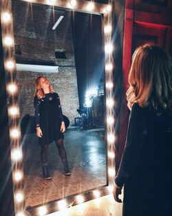 Rear view of woman standing by illuminated lamp at night