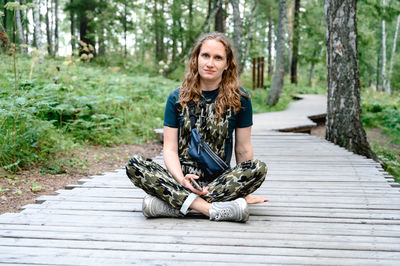 Portrait of young woman sitting on boardwalk in forest
