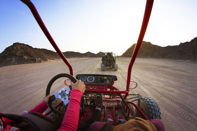 Cropped image of tourists riding beach buggies on dessert against clear sky