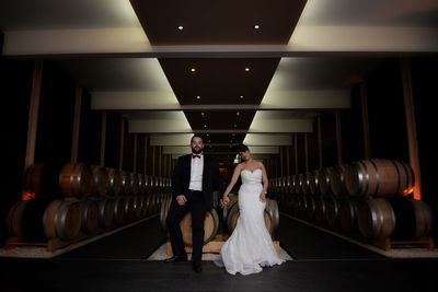 Well dressed bride and groom sitting on barrels in factory