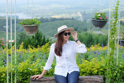 Smiling beautiful woman wearing sunglasses while sitting against plants