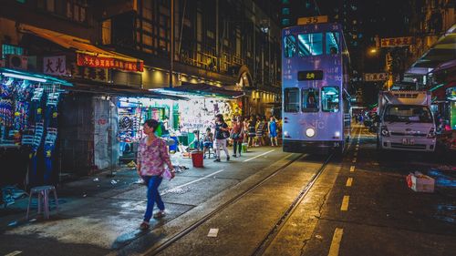 Woman walking on city street by cable car at night