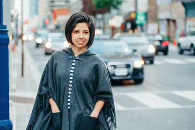 Beautiful latin young woman in grey stylish poncho with fringe in urban street. street fashion 