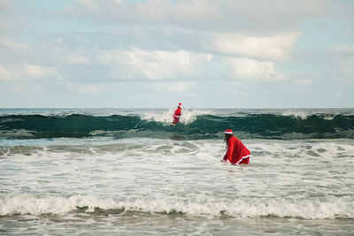 Couple wearing santa costumes surfing on sea