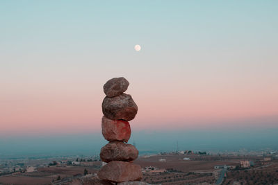 Stack of rocks on shore against sky at sunset