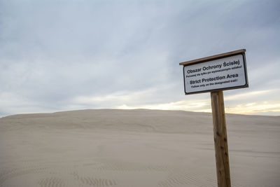 Information sign board on desert against sky