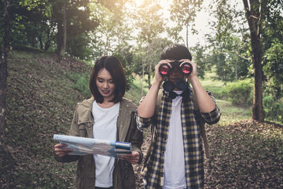 Explorers holding map and binoculars while standing in forest