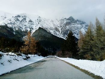 Diminishing perspective of empty road against snowcapped mountain in forest
