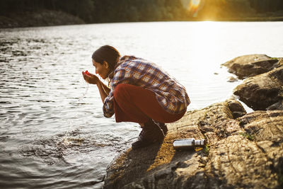 Side view of woman drinking water from lake in forest