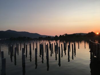 Wooden posts in lake against sky during sunset