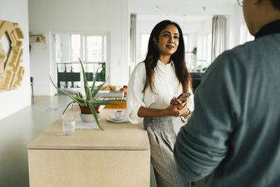 Businesswoman talking to male colleague while leaning on table at office