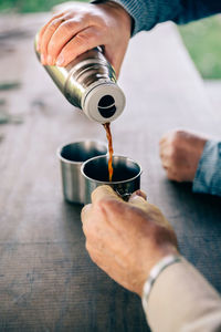 Cropped hand pouring black coffee in cup held by friend