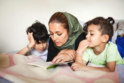 Mother reading book to boys while lying on bed at home