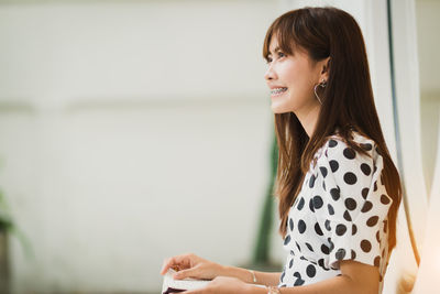 Side view of smiling young woman looking away while reading book