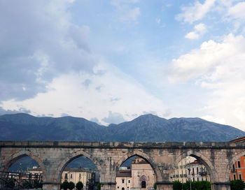 Arch bridge over mountain against cloudy sky