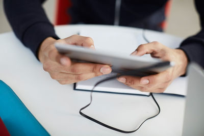 Midsection of university student using digital tablet at table while studying in cafeteria