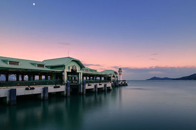 Stilt house by sea against sky during sunset