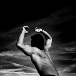 Rear view of shirtless man holding woman against sky