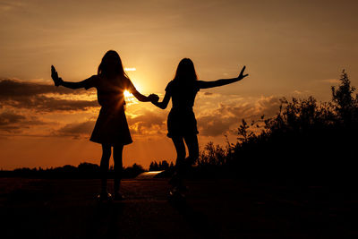 Silhouette friends holding hands standing on land against sky during sunset