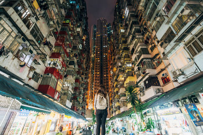 Rear view of woman standing amidst illuminated buildings in city