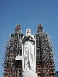 March 2023 statue of mother mary, with the background of notre-dame cathedral undergoing renovation.