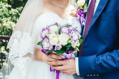 Midsection of bridal couple holding bouquet