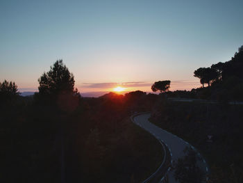 Silhouette trees by road against sky during sunset