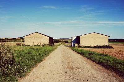 Barn on field by houses against sky